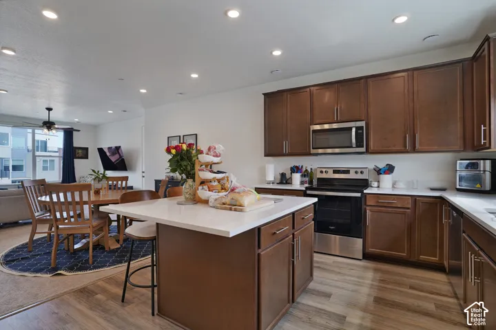 Kitchen featuring wood-finish flooring, white countertops, dark wood-finish cabinetry, and stainless steel appliances