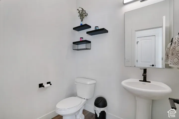 Pedestal sink with matte black faucet, wall-mounted mirror with integrated lighting, floating wall shelves, and wood-finish flooring