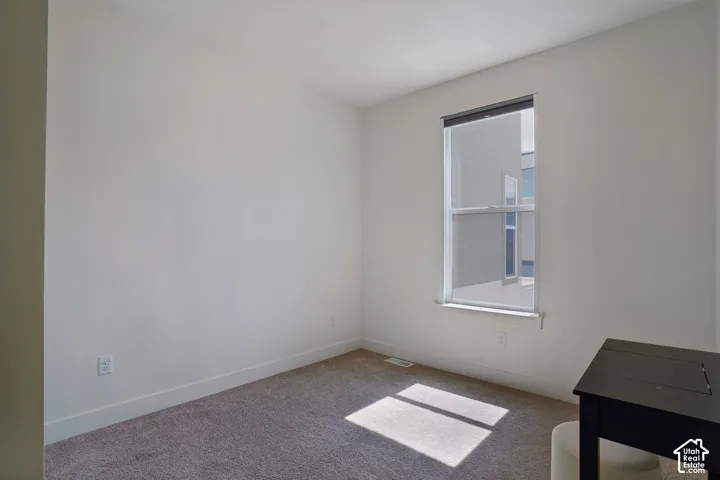 Carpeted flooring, white walls, and a single window with a roller shade