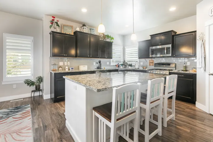 Kitchen featuring an expansive island with a light-toned countertop, dark wood-finish cabinetry, stainless steel appliances, a tiled backsplash, and recessed lighting
