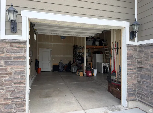 Attached garage with stone veneer accents, exterior wall lanterns, overhead storage, and an interior access door