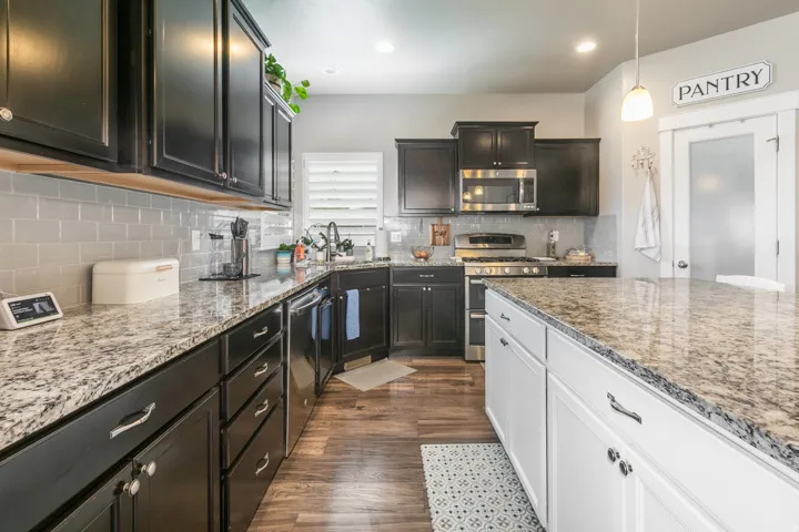 Kitchen featuring stone countertops, dark wood-finish cabinetry, stainless steel appliances, a light-colored subway tile backsplash, and a central island with white cabinetry