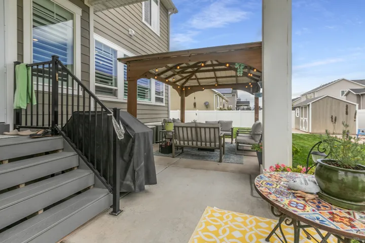 Backyard patio featuring a wood pergola with strung lighting, concrete hardscaping, and a gray composite deck with black metal railings