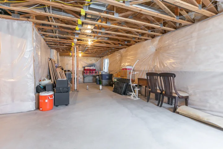 Unfinished basement with exposed ceiling joists, concrete flooring, and vapor barrier-lined walls