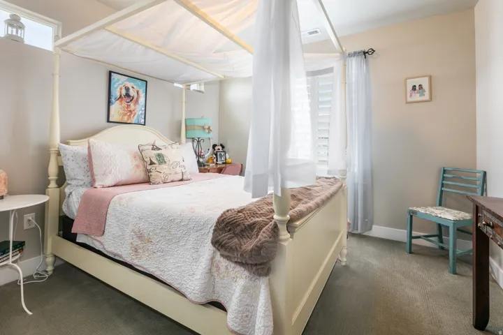 Elegant primary bedroom featuring a four-poster canopy bed frame, soft neutral palette, and abundant natural light from multiple windows