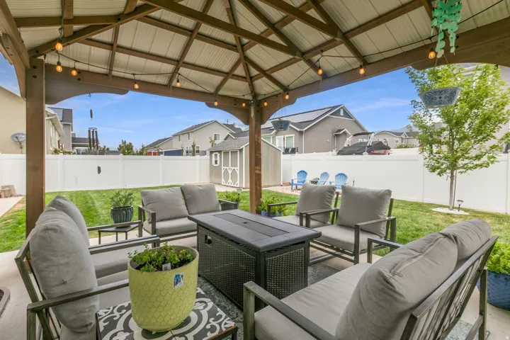 Covered patio with string lighting, expansive lawn, white privacy fencing, and an on-site storage shed