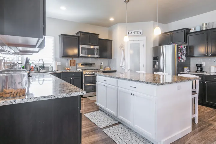 Kitchen featuring dark wood-finish cabinetry, light-toned granite countertops, stainless steel appliances, a central island with white cabinetry, and wood-finish flooring