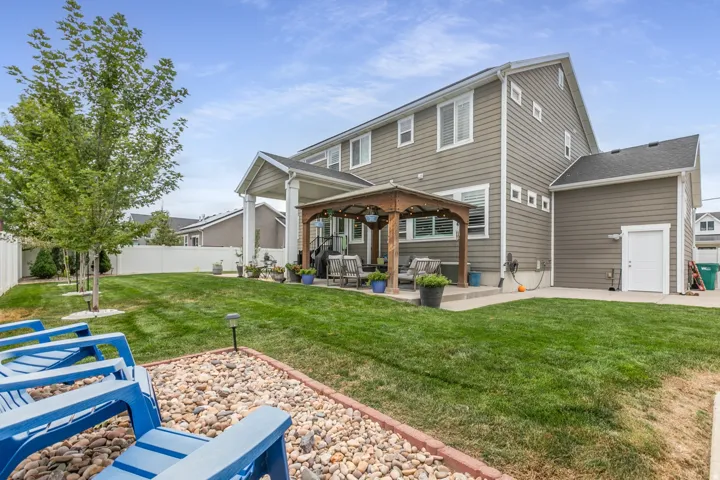 Expansive lawn with mature trees, a covered patio featuring a wooden gazebo, and a fully fenced perimeter