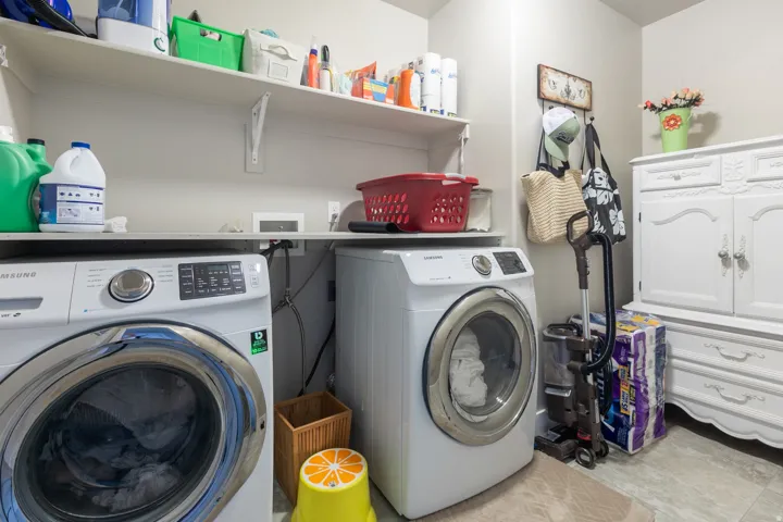 Dedicated laundry room featuring dual front-load washers and dryers, ample shelving for storage, utility sink, and tile flooring