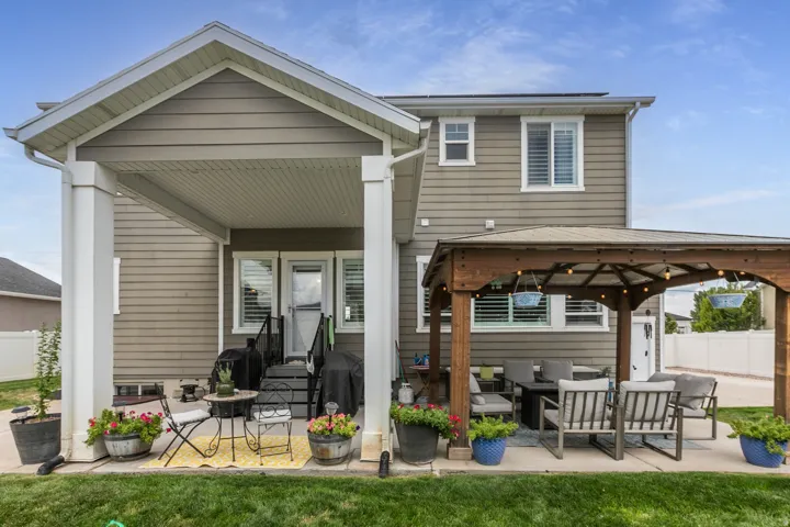 Covered patio with white columns, wood siding exterior, gazebo with string lights, concrete patio, and green lawn