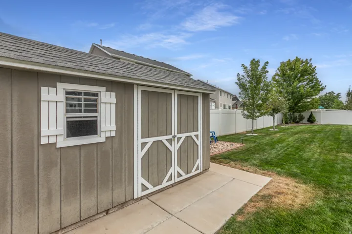 Storage shed with a shingled roof, double entry doors, a window with shutters, and a concrete pad