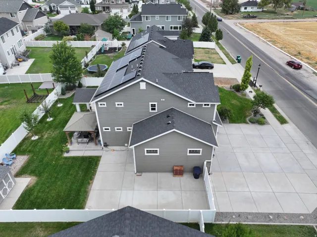 Gray horizontal siding, white trim accents, dark shingle roofing, integrated solar panels, and a covered patio structure