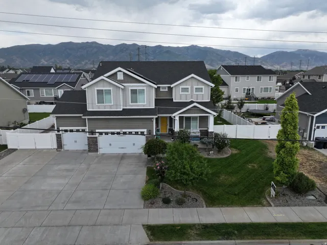 Two-story residence with a gray and light siding exterior, a multi-car concrete driveway, a manicured lawn, and a white privacy fence