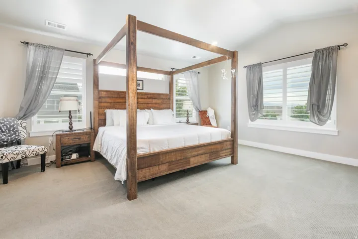 Vaulted ceiling, two large windows, white plantation shutters, light-toned carpeting, and neutral wall color