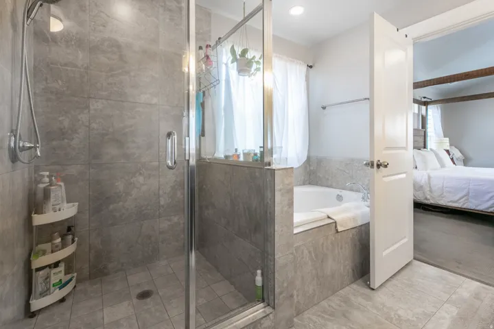 Spacious bathroom featuring a glass-enclosed shower, built-in soaking tub, and floor-to-ceiling gray tile