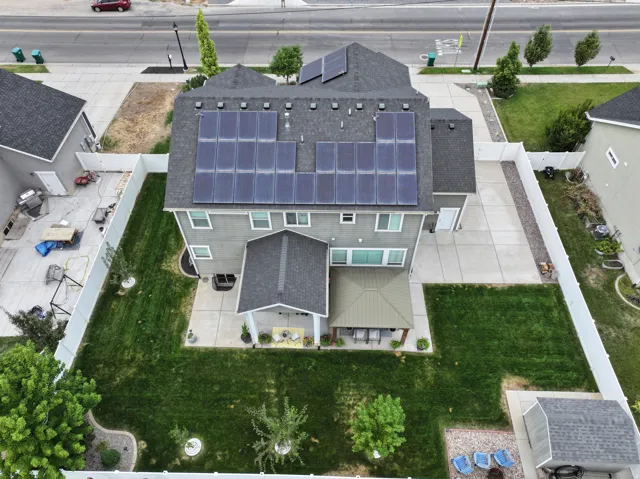 Rear exterior featuring a covered patio, multiple solar panel arrays, a concrete patio, a manicured lawn, and a storage shed
