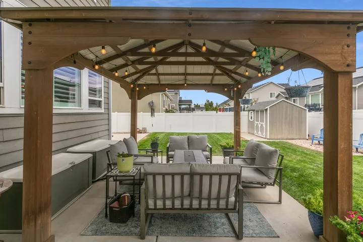 Covered patio with string lighting, wood-finish gazebo, concrete flooring, and a fenced backyard with a storage shed