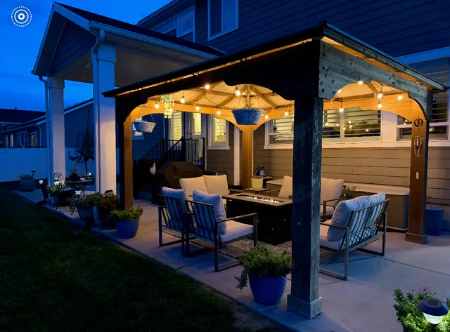 Spacious concrete patio featuring a wood pergola with string lighting, a built-in fire pit, and a covered porch area