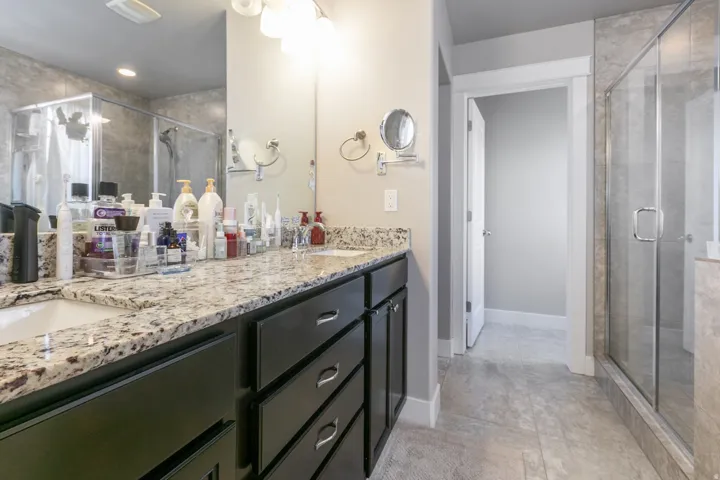 Dual vanity with undermount sinks, granite countertops, dark wood-finish cabinetry, and a glass-enclosed shower with tile surround