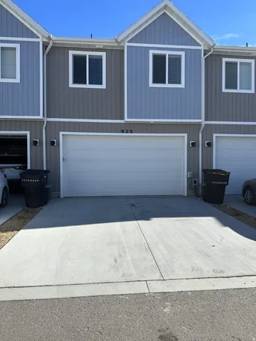 Two-story townhouse exterior with vertical siding, gable accents, white-framed windows, attached garage, and concrete driveway