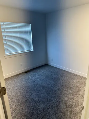 Wall-to-wall carpeting in a neutral tone, white walls, and a window with horizontal blinds