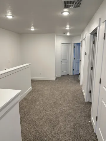 Recessed lighting, neutral carpeting, white interior doors, and crisp white walls