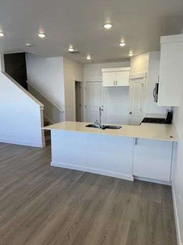 Kitchen featuring an island with an undermount double-basin sink, stainless steel faucet, white cabinetry, and light-toned countertops
