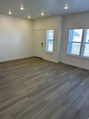 Wood-finish flooring, white walls, recessed ceiling lighting, and multiple windows with blinds