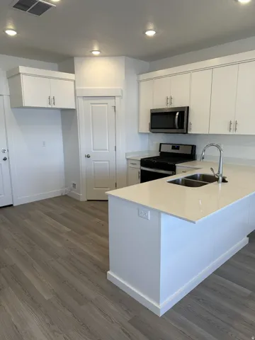 Kitchen featuring an island with an undermount double-basin sink, stainless steel appliances, white cabinetry, and wood-finish flooring