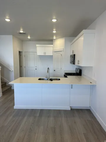 Kitchen featuring recessed lighting, white cabinetry, a kitchen island with an undermount double-basin sink, light-toned countertops, and wood-finish flooring