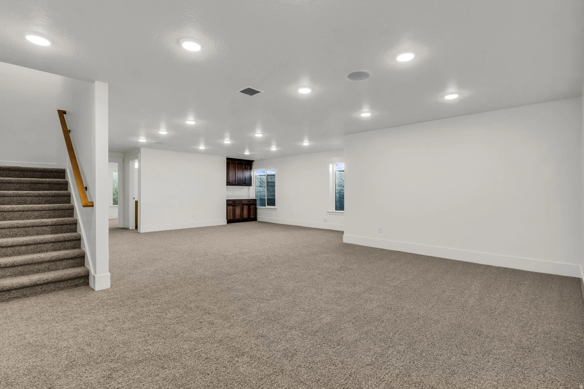 Expansive carpeted room with recessed lighting, integrated ceiling speakers, and built-in cabinetry featuring dark wood finishes