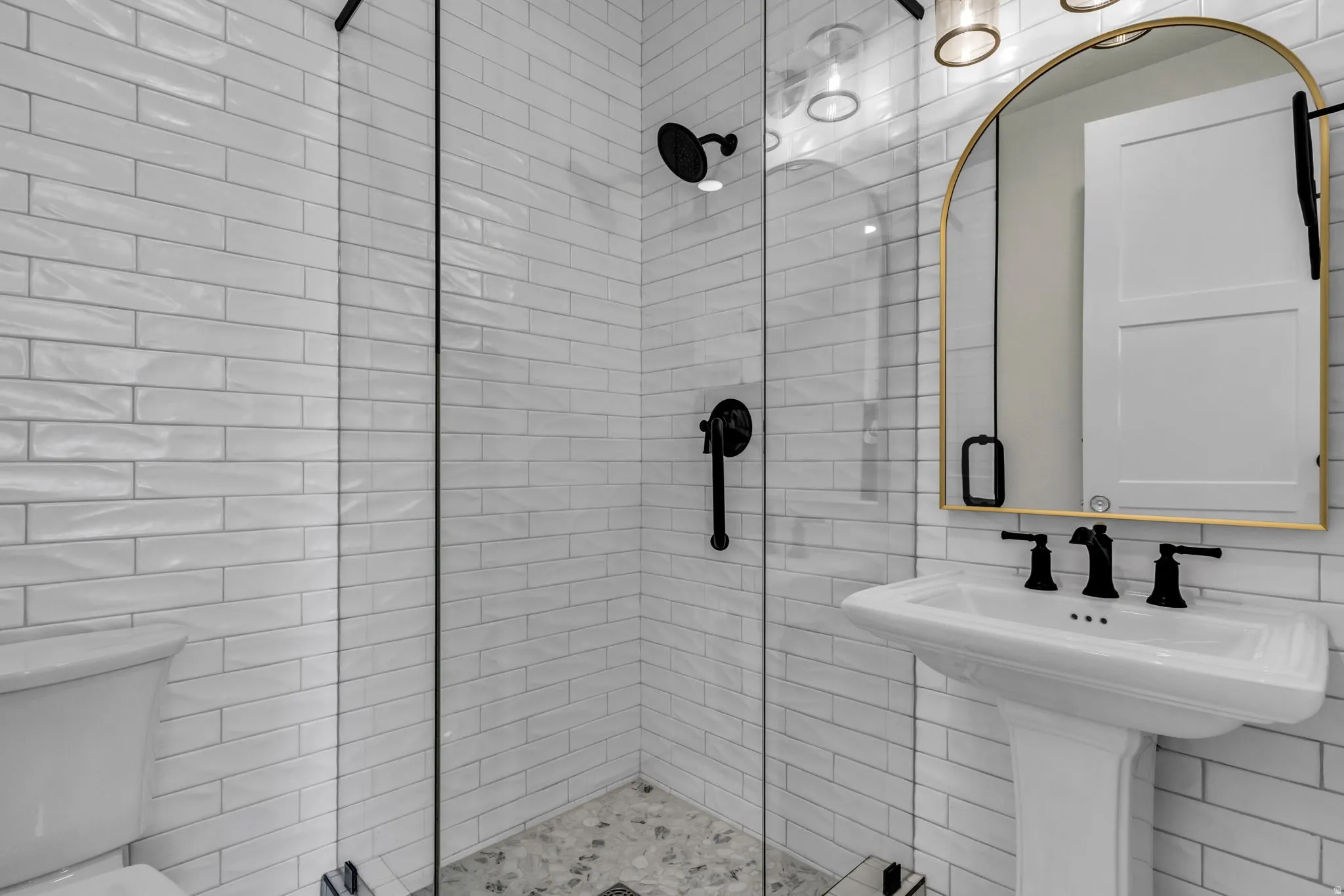 Glass-enclosed shower with white subway tile, pebble tile shower floor, and matte black fixtures