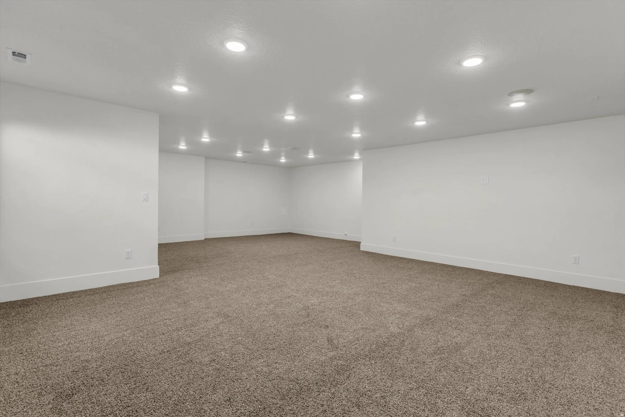Spacious room featuring neutral carpeting, recessed lighting, and crisp white walls