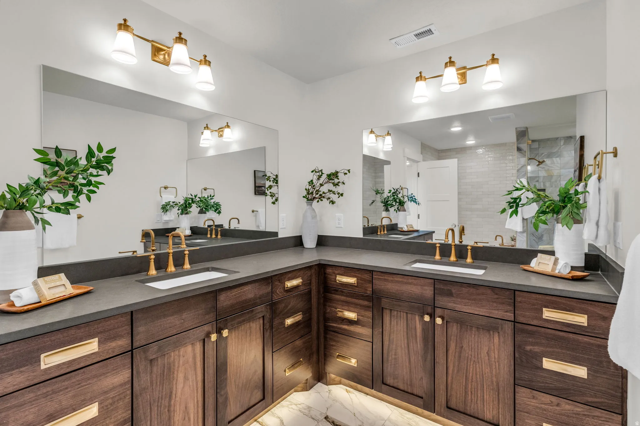Dual vanity with dark wood-finish cabinetry, integrated sinks, dark countertops, and gold-tone hardware