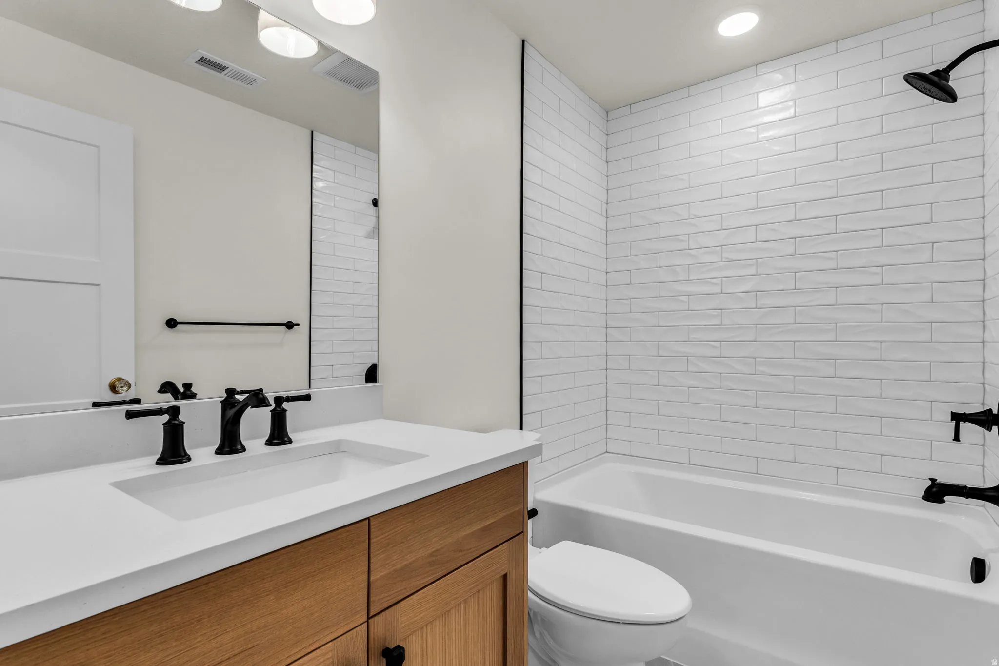 Bathroom featuring a wood-finish vanity with a white countertop, matte black fixtures, an integrated sink, and white subway tile in the shower area