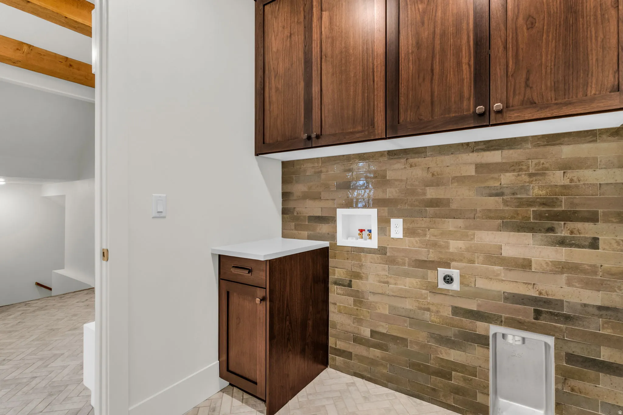 Wood-finish cabinetry, stone tile accent wall, white countertop, and herringbone pattern floor tile