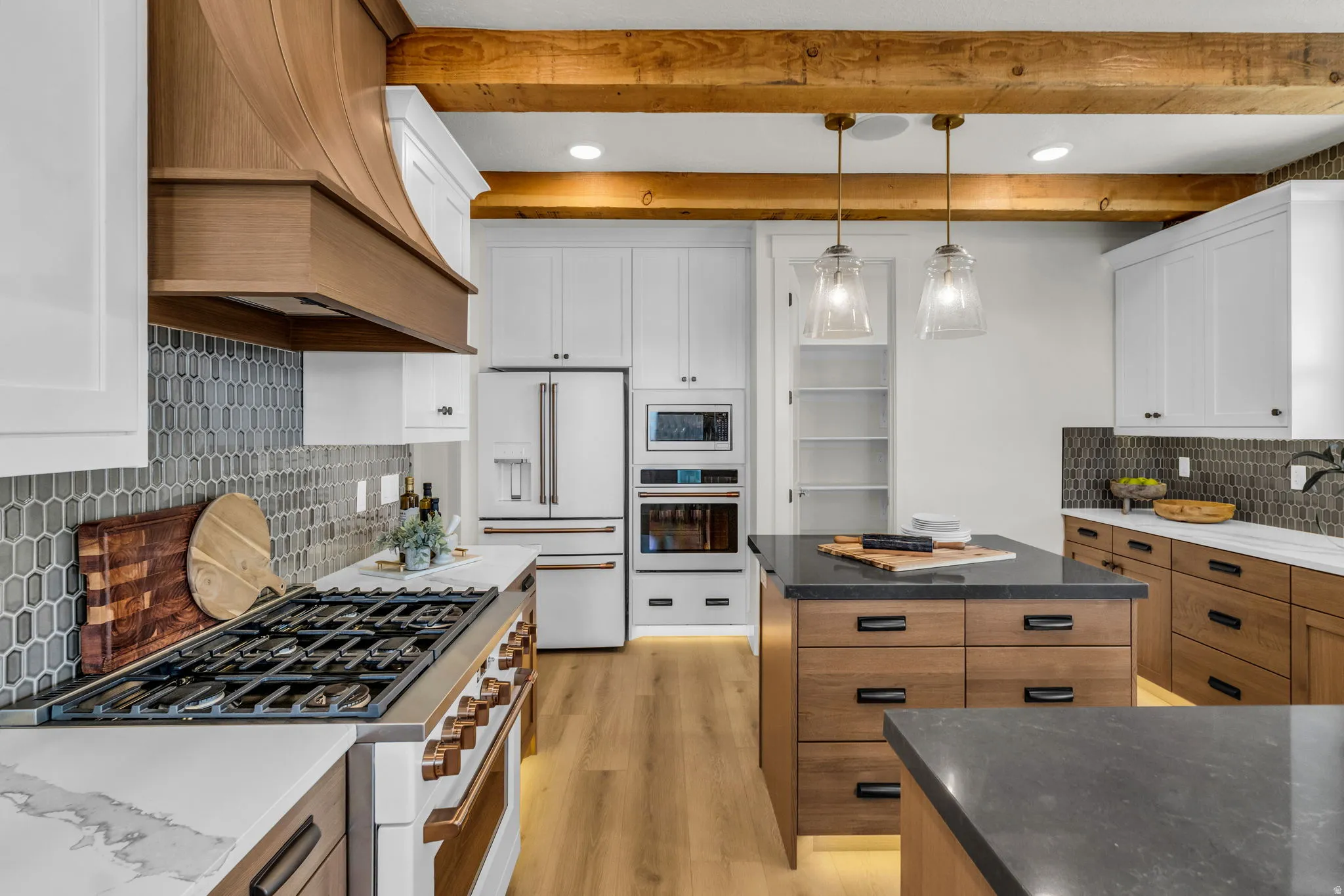 Modern kitchen featuring a gas range, wood-finish flooring, white and wood cabinetry, a center island with a dark countertop, and exposed wood beams
