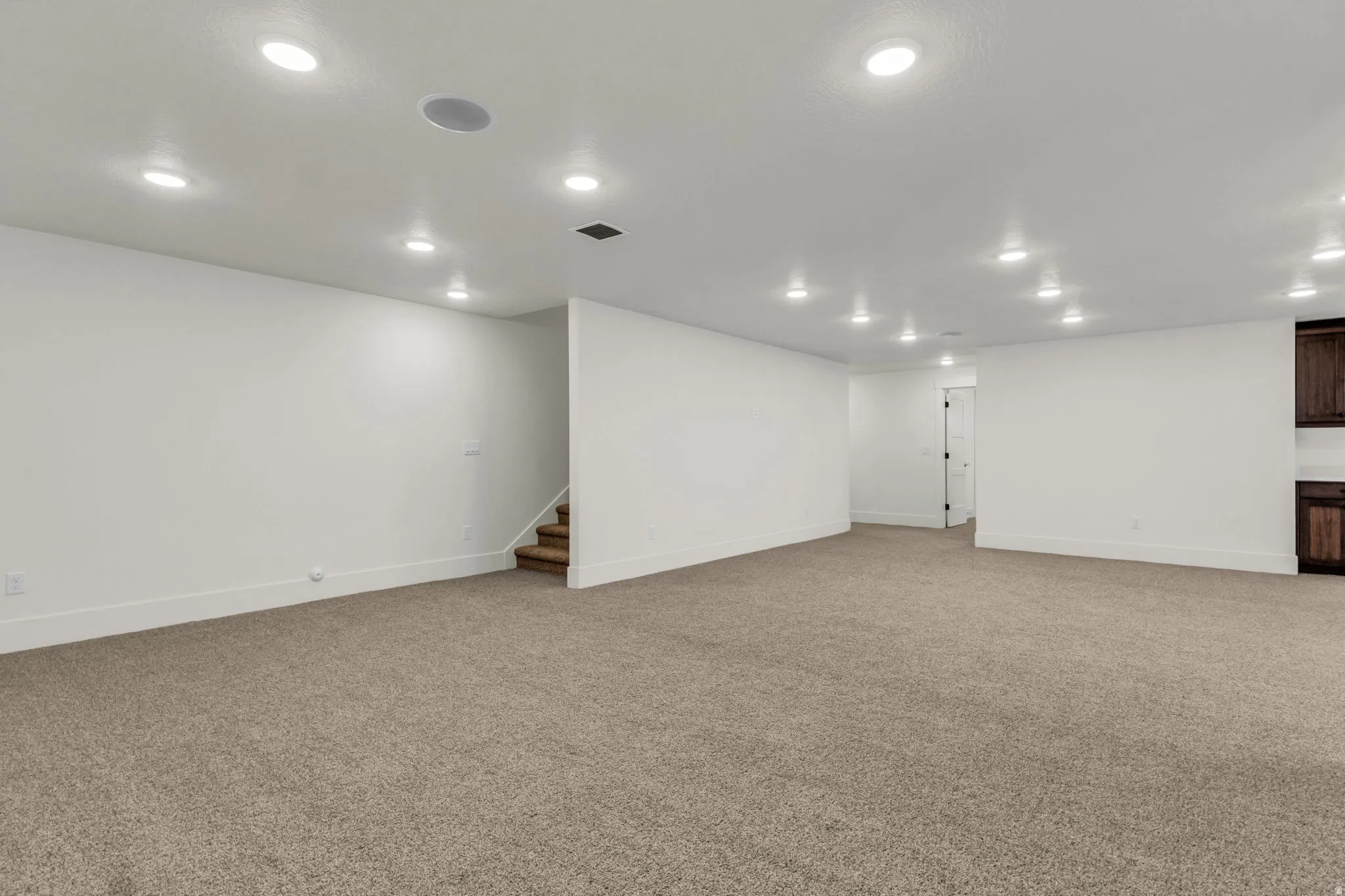 Expansive carpeted area with recessed lighting, integrated ceiling speakers, and light-toned walls