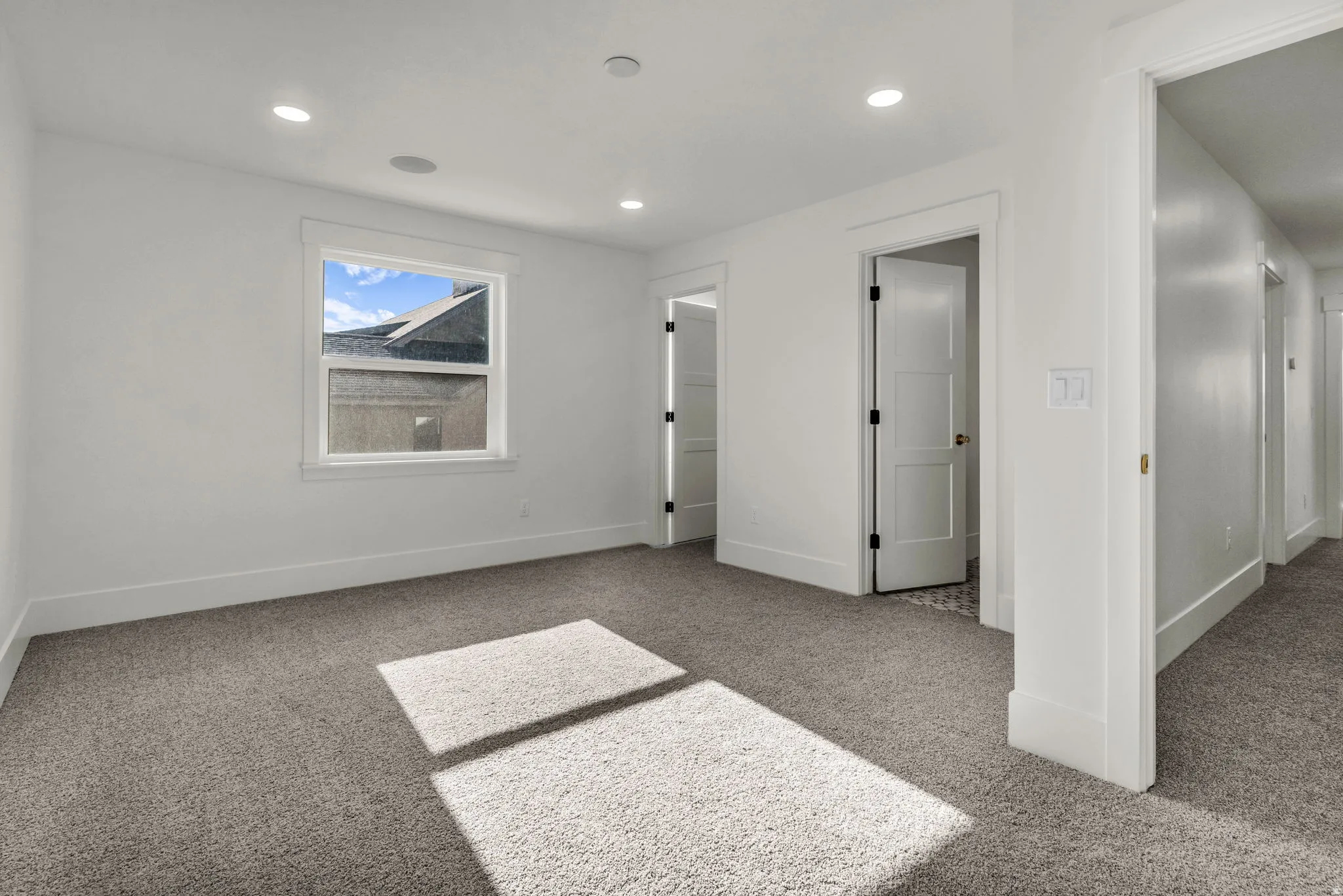 Recessed lighting, textured carpet flooring, white trim details, white interior doors, and a window with white casing