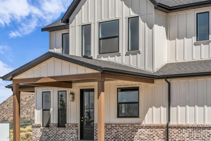 Board and batten siding with a brick foundation, a covered porch with wood-finish columns, and a dark shingle roof