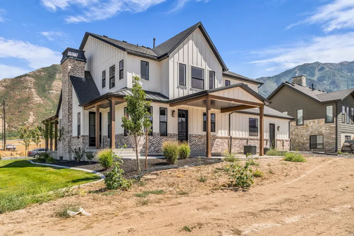 Modern farmhouse exterior featuring board-and-batten siding, a prominent brick chimney, and a covered porch with timber accents