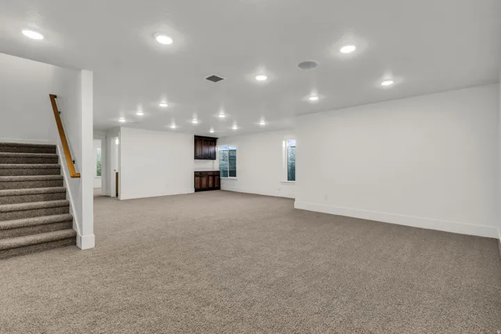 Expansive carpeted room with recessed lighting, integrated ceiling speakers, and built-in cabinetry featuring dark wood finishes