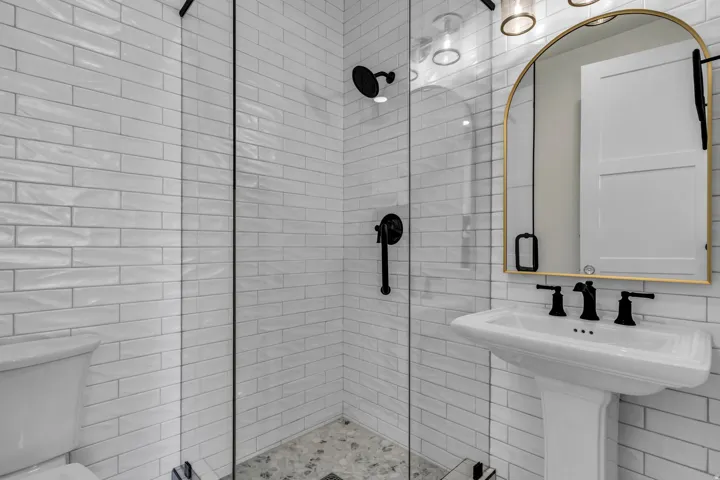Glass-enclosed shower with white subway tile, pebble tile shower floor, and matte black fixtures
