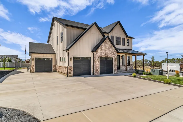 Two-story exterior featuring board and batten siding, brick accents, multiple gables, a covered porch with wood columns, and three garage bays with dark doors