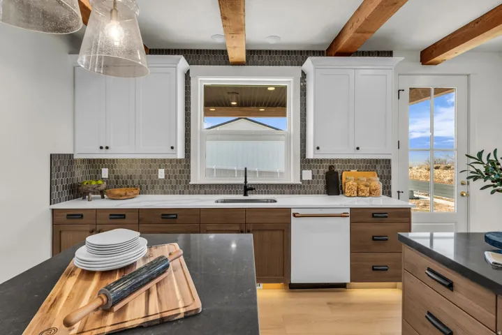 Kitchen featuring exposed wood beams, white upper cabinetry, wood-finish lower cabinetry, a built-in dishwasher, and a patterned tile backsplash