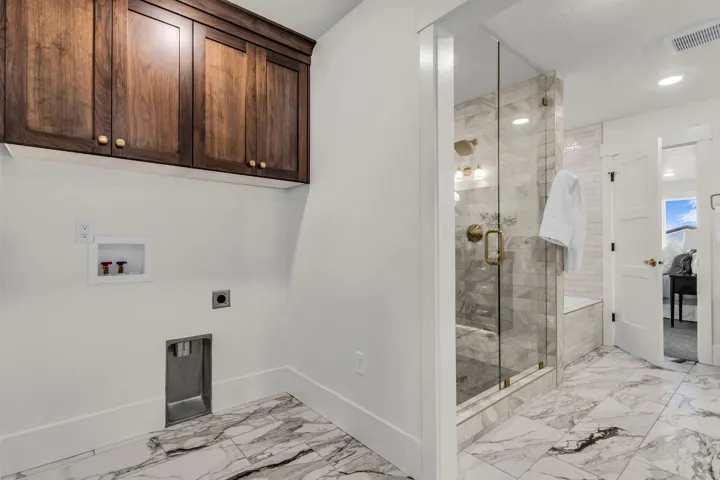 Spa-inspired primary bathroom featuring a frameless glass-enclosed walk-in shower with marble-finish tile surround, marble-finish flooring throughout, custom wood cabinetry with polished hardware, and recessed ceiling lighting