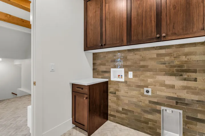 Wood-finish cabinetry, stone tile accent wall, white countertop, and herringbone pattern floor tile