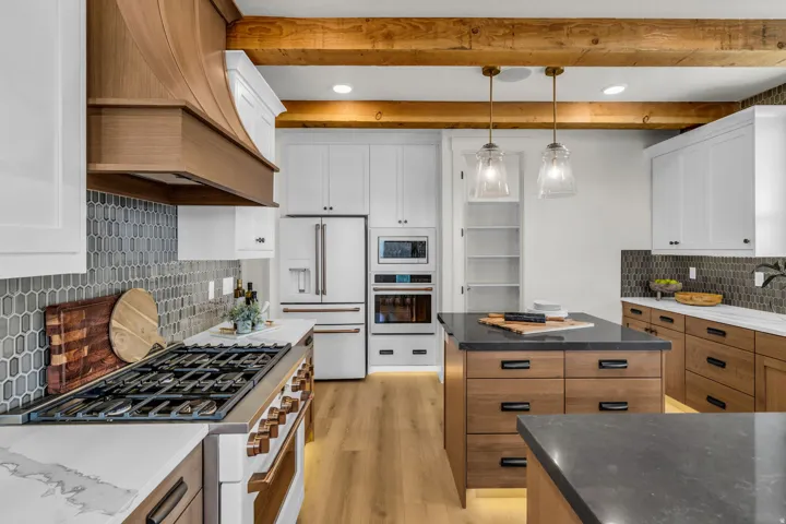 Modern kitchen featuring a gas range, wood-finish flooring, white and wood cabinetry, a center island with a dark countertop, and exposed wood beams