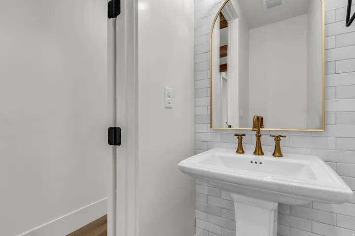 Pedestal sink, wall-mounted faucet, subway tile, arched mirror, and brass-finish fixtures