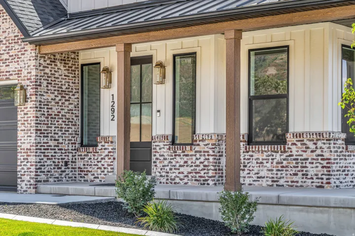 Front elevation featuring a mixed-material facade with brick and vertical siding, a covered entryway with wood-finish posts, and a black paneled front door